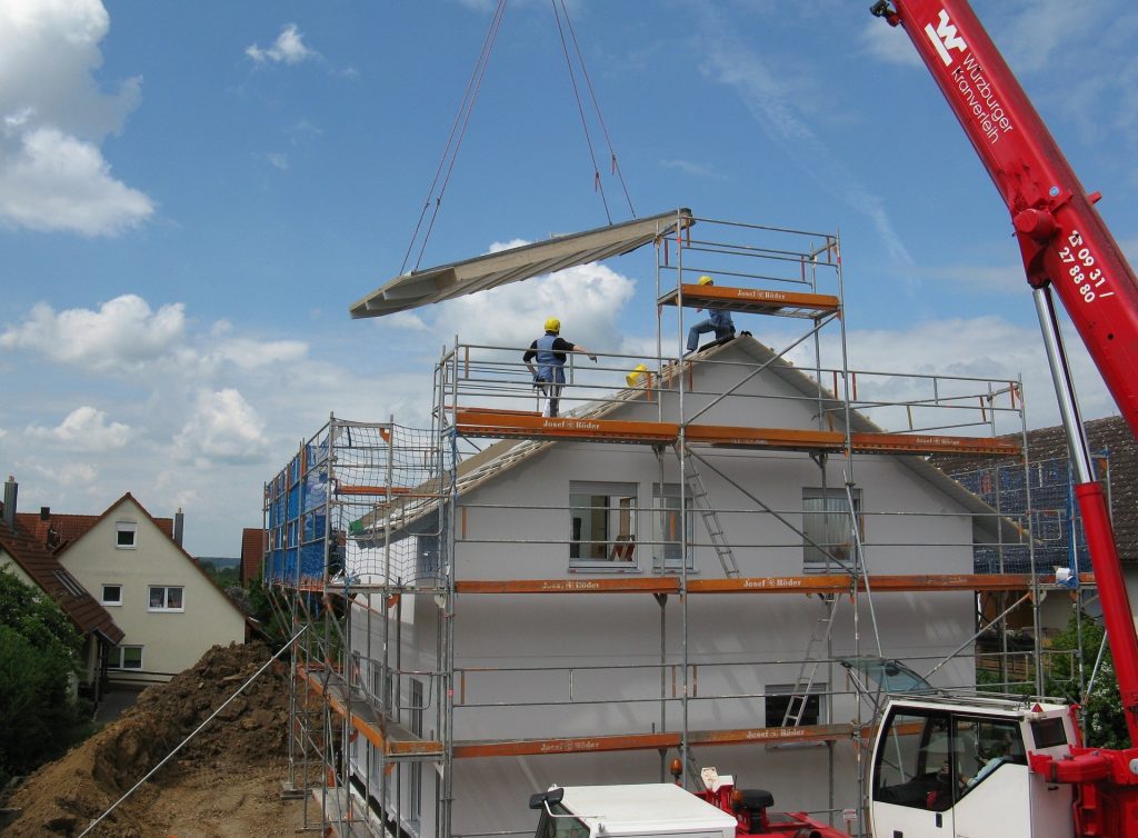 Un maison en construction avec un camion grue et installation de toiture